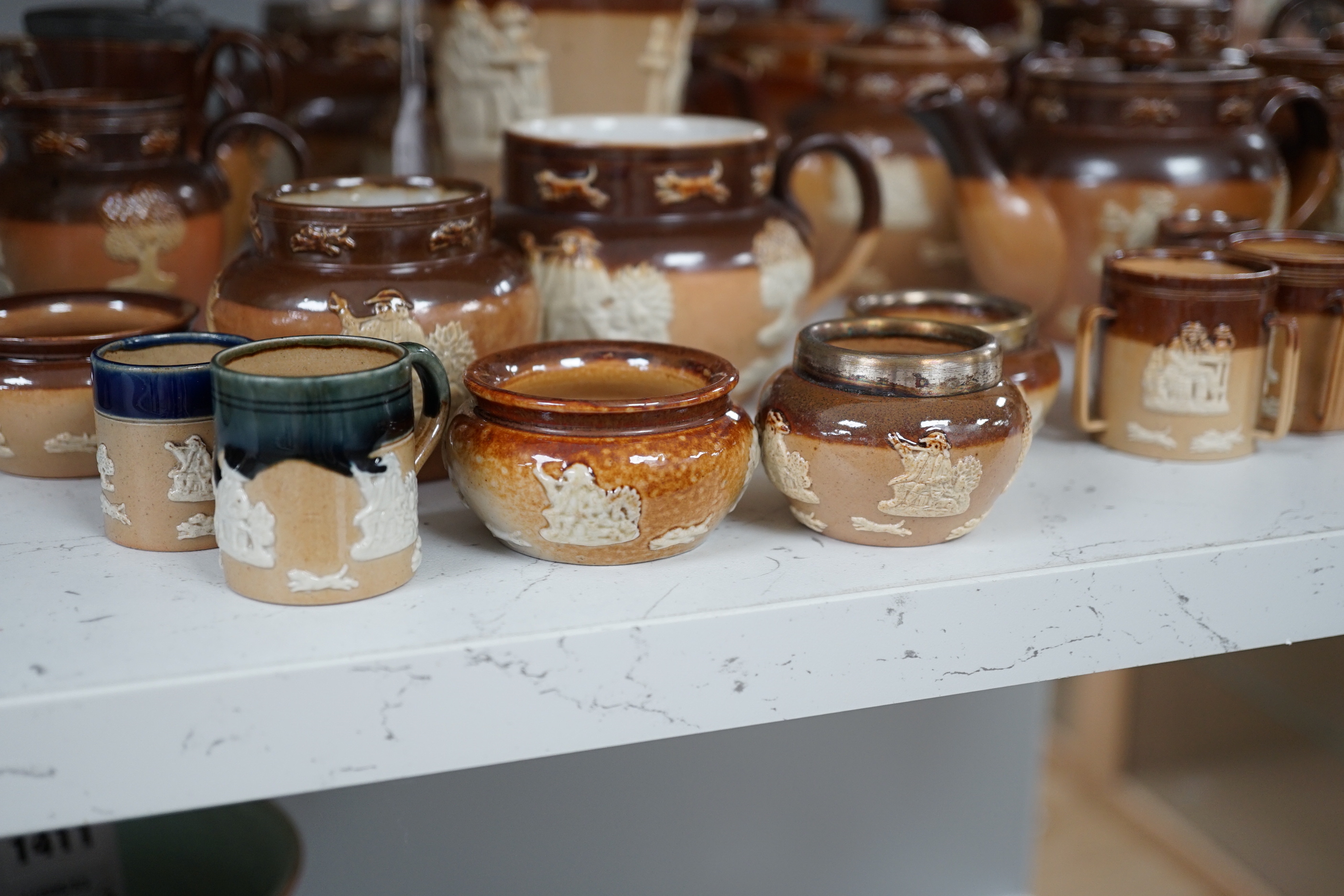 An assortment of Doulton stoneware including teapots, miniature tygs and twin handled pots, some silver mounted, largest 22cm wide